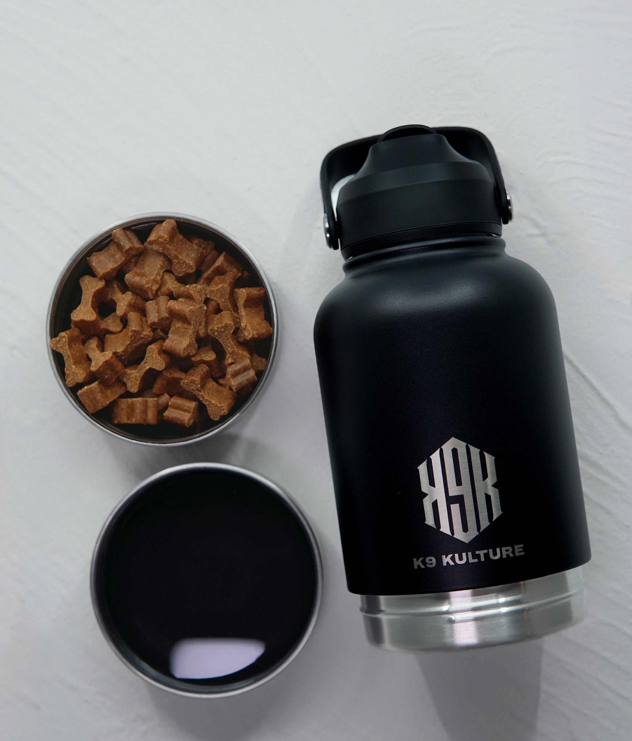 Black ThermoACTIVE insulated dog water bottle displayed with dual compartments—one filled with water, one with treats.